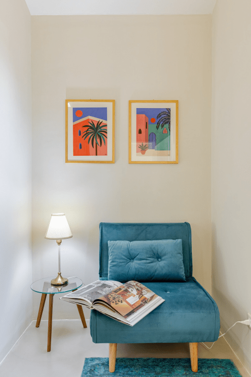 Poltrona turchese con rivista nell'appartamento Case Luparello, arredato con quadri colorati e lampada da tavolo in ottone.