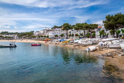 Playa de Llafranc con barcas coloridas, orilla arenosa y edificios blancos mediterráneos bajo cielo azul