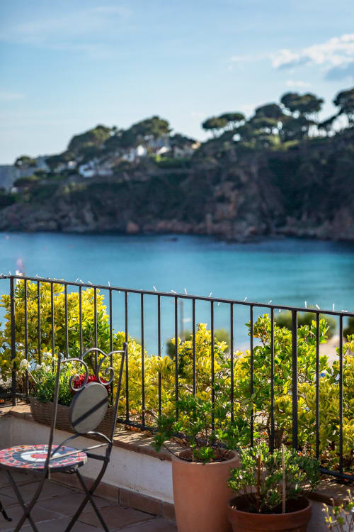 Terraza del Hotel La Muntanya con vistas a una cala turquesa del Mediterráneo, flores amarillas y acantilados costeros