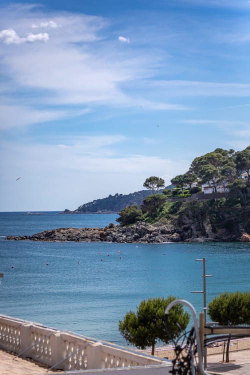 Cala de aguas cristalinas en el Mediterráneo con costa rocosa, embarcaciones fondeadas y villa de lujo en la ladera de Llafranc, España