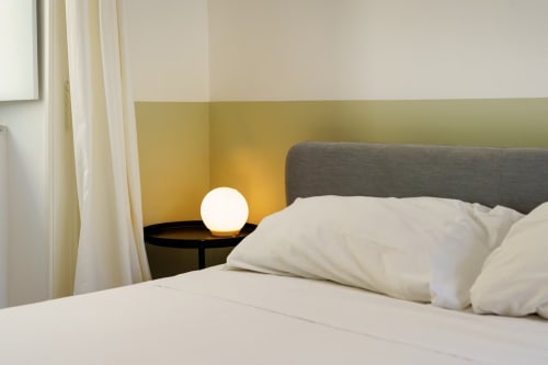 Camera moderna a B&B Oliveri 25 a Procida con testata grigia, biancheria bianca, parete gialla e comodino luminoso