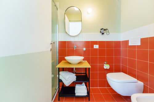 Bagno moderno con piastrelle rosse, lavabo bianco su colonna, wc e mobile legno in B&B Oliveri 25 a Procida