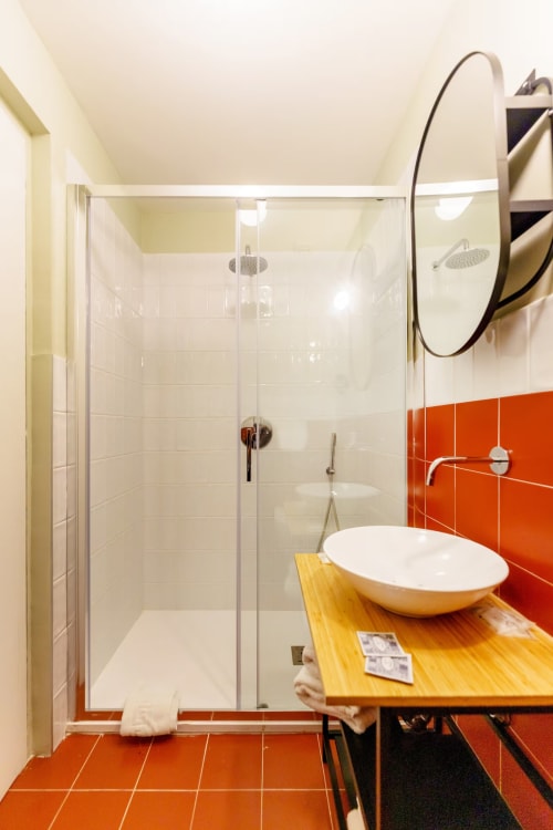 Bagno moderno al B&B Oliveri 25 di Procida con doccia in vetro, lavabo bianco, piastrelle arancioni e specchio rotondo