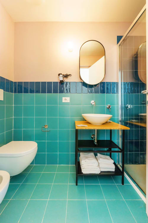 Bagno moderno della B&B Oliveri 25 a Procida con piastrelle turchesi, lavabo bianco, specchio ovale e vanità nera