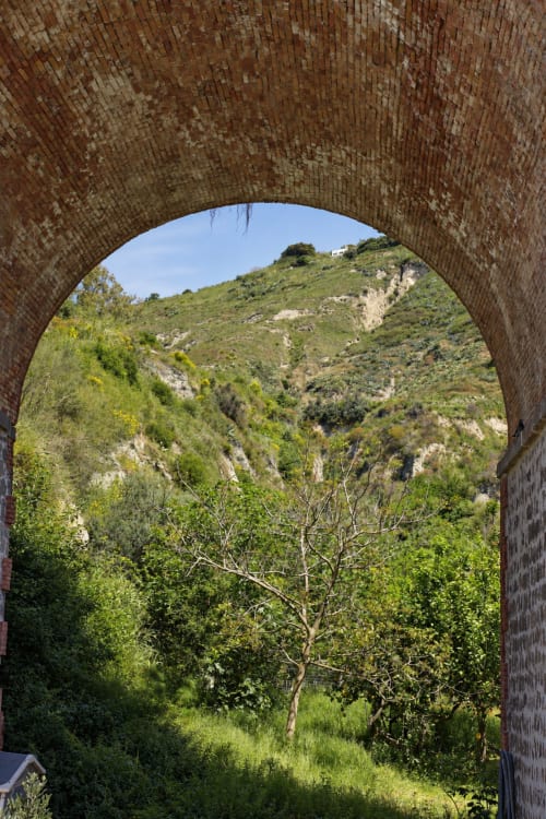 Corridoio ad arco in mattoni che incornicia la verdeggiante collina con ulivo, giardino Villa Bina Sea Hotel, Serrara Fontana