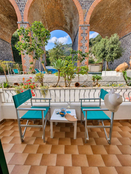 Sedie turchesi affacciano su un'architettura con volta in mattoni nel giardino del Villa Bina Sea Hotel a Serrara Fontana