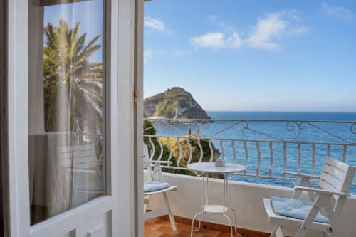 Vista dal balcone del Mar Mediterraneo blu e montagna a Villa Bina Sea Hotel, Serrara Fontana con lettini bianchi e palme