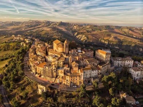 Villaggio medievale in collina con edifici in pietra dorata e torre della chiesa, paesaggio della campagna toscana al tramonto