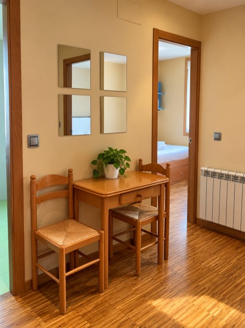 Acogedor espacio de trabajo en apartamento de Baiona con escritorio de madera, silla, espejos, planta en maceta y puerta abierta al dormitorio