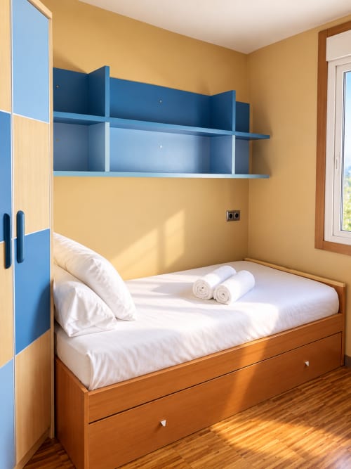 Luminoso dormitorio en apartamento de Baiona con cama de madera, estantería azul, paredes amarillas y ropa de cama blanca