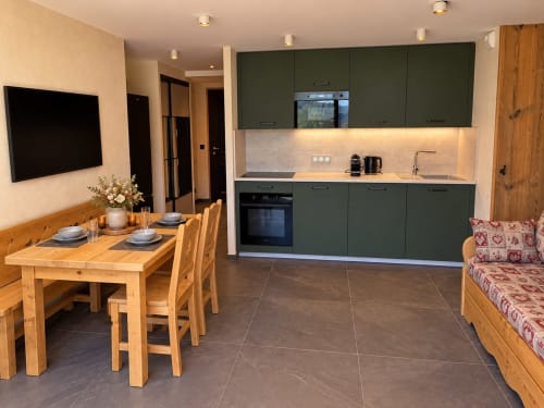 Cuisine moderne et coin repas aux Tanières de Montgenèvre avec mobilier vert, table en bois et vue montagne