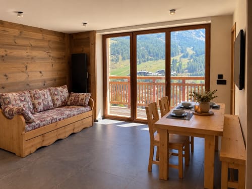 Salon d'appartement avec vue montagne, mobilier en bois, table à manger, canapé et balcon panoramique