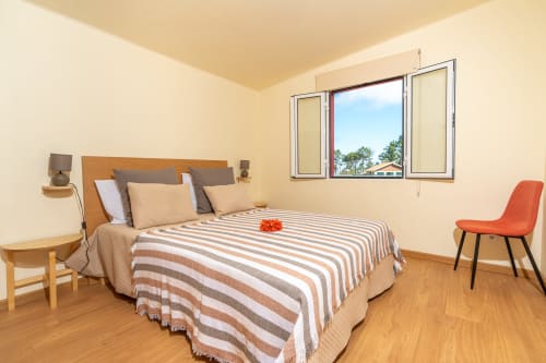 Bright bedroom at Quinta Frizado in Prazeres with striped bedding, wooden headboard, modern chair, and garden views