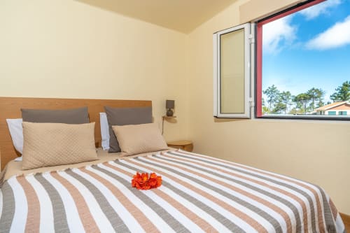 Bright bedroom at Garry's Holiday Rentals in Prazeres with striped bedding, wood headboard, and garden view through window
