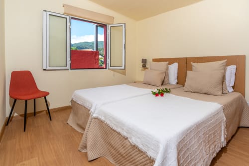Bright bedroom at Garry's Holiday Rentals in Prazeres with two beds, red chair, and mountain view through window