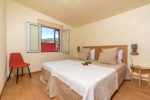 Bright bedroom at Garry's Holiday Rentals in Prazeres with twin beds, wooden furniture, red chair, and mountain view through