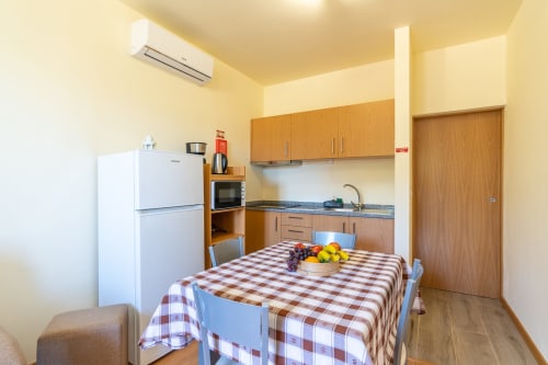 Modern kitchenette with dining table, white refrigerator, and wooden cabinetry at Quinta Frizado apartment in Prazeres,