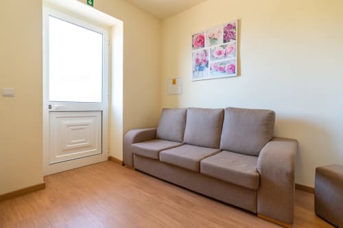 Cozy living room at Garry's Holiday Rentals in Prazeres with taupe sofa, yellow walls, floral artwork, and glass door