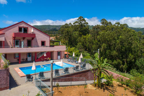 Garry's Holiday Rentals in Prazeres: red apartment with pool, lounge chairs, umbrellas, mountain views and eucalyptus forest.