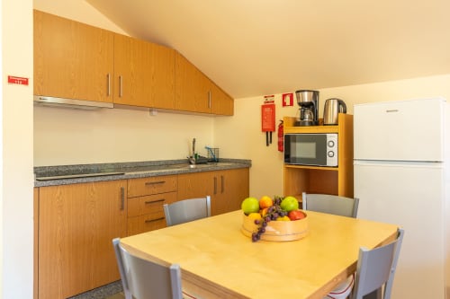Modern kitchenette with wooden cabinets, yellow dining table, fresh fruit bowl, and appliances at Garry's Holiday Rentals