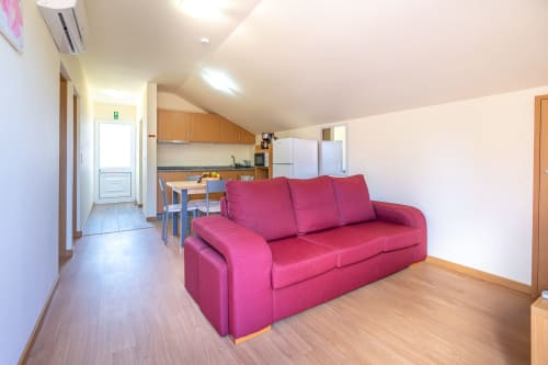 Bright open-plan living area with magenta sofa, kitchenette, and dining table at Quinta Frizado apartment, Prazeres Portugal