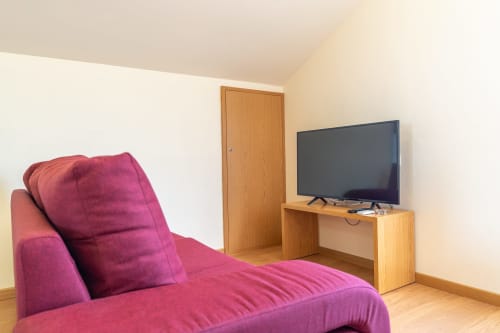 Magenta sofa with pillows, wooden TV stand with flat-screen TV, and wooden door in bright apartment living area at Garry's
