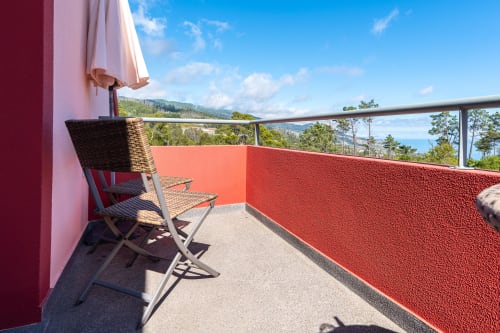 Sunny balcony with wicker chair and red terrace overlooking mountains at Quinta Frizado, Prazeres Portugal