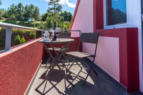 Sunny balcony at Quinta Frizado apartment in Prazeres with sea view, outdoor dining table, chairs, wine, and forest backdrop