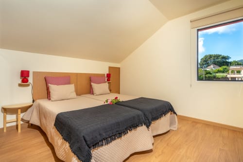 Modern bedroom with twin beds, wooden headboard, red accents, and garden views at Garry's Holiday Rentals in Prazeres