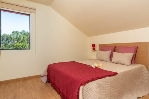 Bright bedroom at Garry's Holiday Rentals in Prazeres with queen bed, red throw, wooden flooring, and garden view window