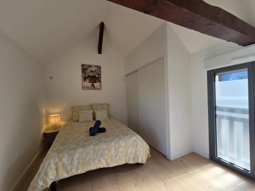 Dormitorio luminoso con cama queen, balcón con vista al lago y techo con vigas oscuras en el apartamento La Perle du Léman, Douvaine