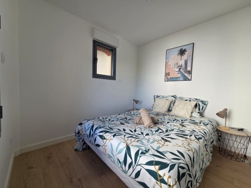 Dormitorio luminoso en NN Patrimoine Douvaine con ropa de cama estampada, suelo de madera, ventana y arte tropical