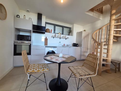 Moderna cocina-comedor del apartamento La Perle du Léman en Douvaine, con muebles blancos, mesa de comedor y escalera