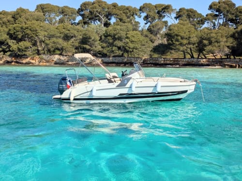 Bateau blanc mouillé dans les eaux turquoise méditerranéennes près de Cagnes-sur-Mer, France, avec pins et littoral rocheux.