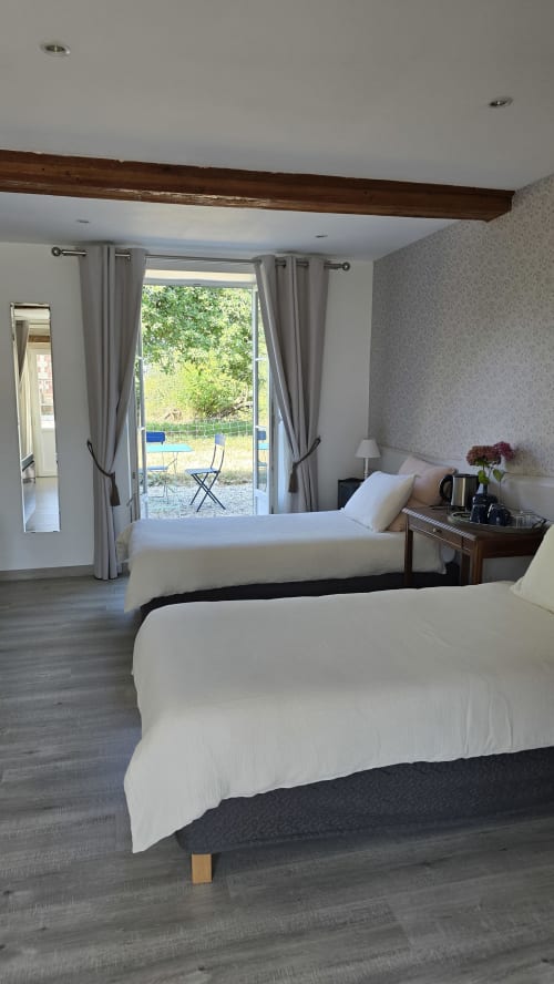 Spacious bedroom with two beds, exposed beam, and French doors opening to garden terrace at Domaine de la Cour VAUTIER in