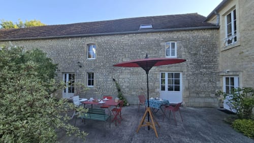 Stone farmhouse patio at Domaine de la Cour Vautier with red umbrella and dining tables in Mandeville-en-Bessin