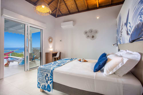 Spacieuse chambre de villa avec vue sur mer, lit king-size, accents bleus, terrasse extérieure, piscine et décor tropical aux Terrasses du Morne
