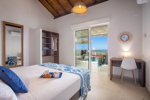 Chambre lumineuse de villa avec vue mer, literie bleue à motifs, accents bois et terrasse donnant sur Le Marin, Martinique