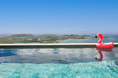 Flotteur flamant rose dans la piscine à débordement surplombant la baie turquoise et les îles verdoyantes de la villa Terrasses du Morne Gommier
