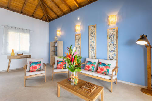 Salon de la Villa Nid des Colibris aux murs bleus, mobilier en bois, fleurs tropicales et vue sur mer aux Terrasses du Morne