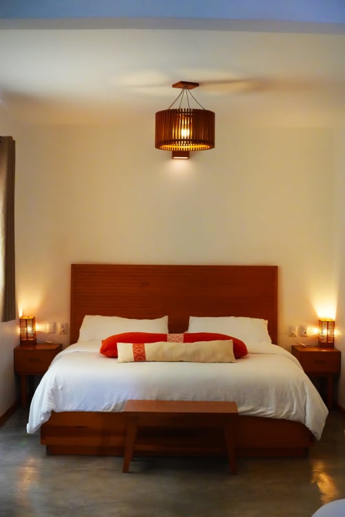 Dormitorio moderno en Casa Cafeólogo con cama de madera, sábanas blancas, detalles rojos, lámpara colgante y lámparas de cabecera