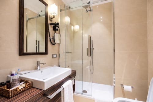 Bagno moderno di Maison Candia B&B Roma con lavabo bianco, doccia in vetro, piastrelle beige e specchio incorniciato