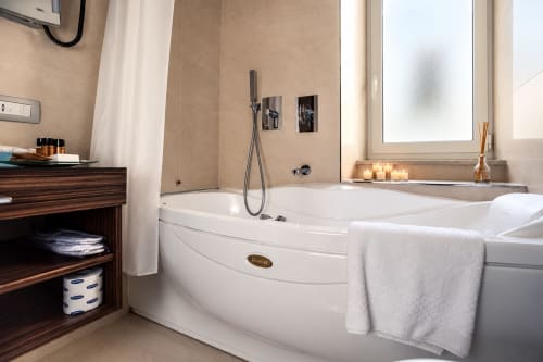 Lussuoso bagno di Maison Candia Roma con vasca bianca, soffione a cascata e finestre con vista sulla città