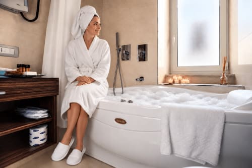 Woman in white robe relaxing in luxury jacuzzi bathtub at Maison Candia Roma deluxe room with city view
