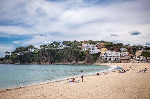 Playa de Llafranc con edificios coloridos, arena dorada y aguas turquesas del Mediterráneo bajo cielo azul