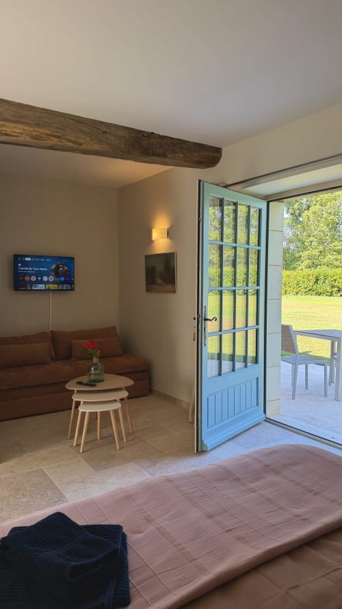 Séjour moderne du gîte Cloffy à Nouans-les-Fontaines avec canapé marron, poutre en bois, téléviseur et portes ouvertes sur la terrasse du jardin