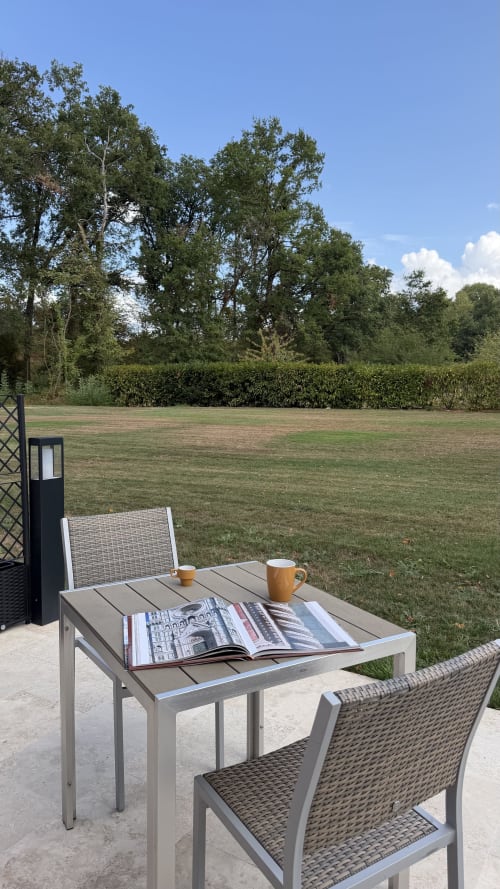 Terrasse extérieure de la Cloffy B&B à Nouans-les-Fontaines avec table, magazine, tasse de café et vue sur le jardin