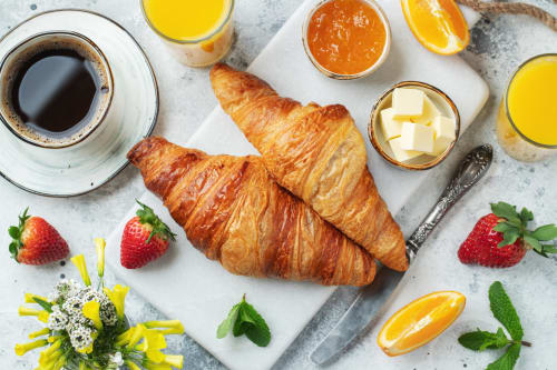 Elegant French breakfast spread with croissants, coffee, orange juice, jam, butter, strawberries and flowers at L'Echappée