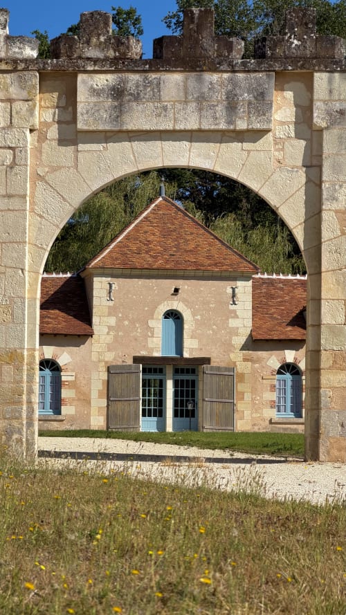 Stone archway framing La mare room at Cloffy B&B in Nouans-les-Fontaines with red-roofed building and lake views