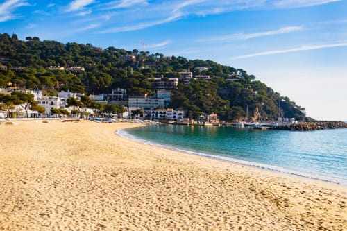 Playa de arena con aguas turquesas y edificios frente al mar entre colinas boscosas en Llafranc, España